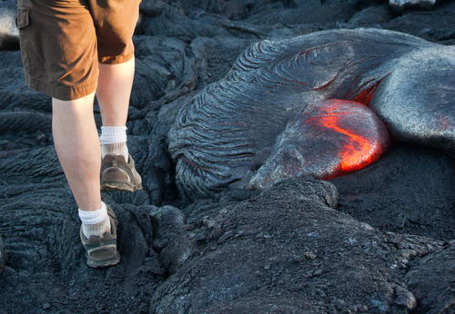 Hiker standing on the lava field near active lava flow, Big Island, Hawaii.