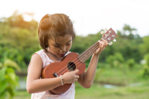 A girl playing on the ukulele from the best Hawaiian island to visit for kids.