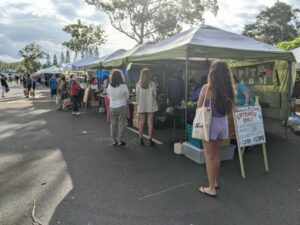 People standing in line for one of the fresh vegetable booths at the farmers' market at Mililani High School.