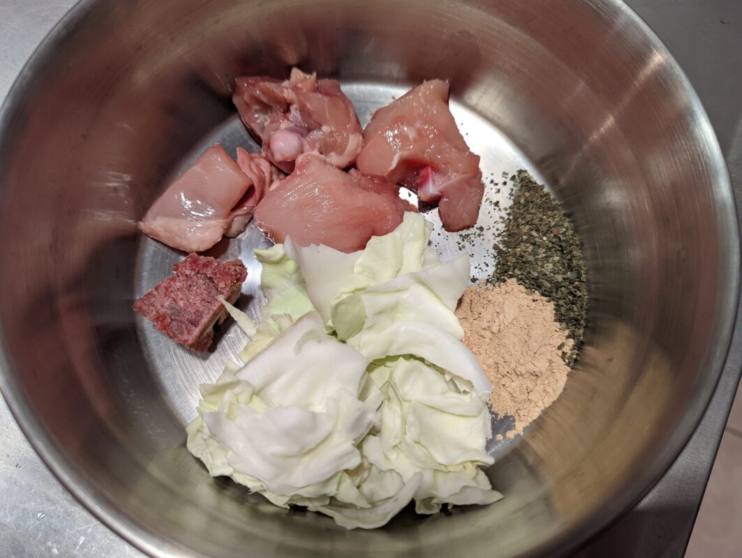 A bowl of raw chicken and cabbage.