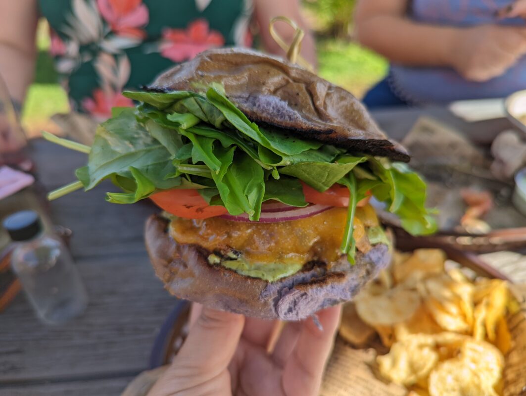 Hand holding a burger with purple bun.