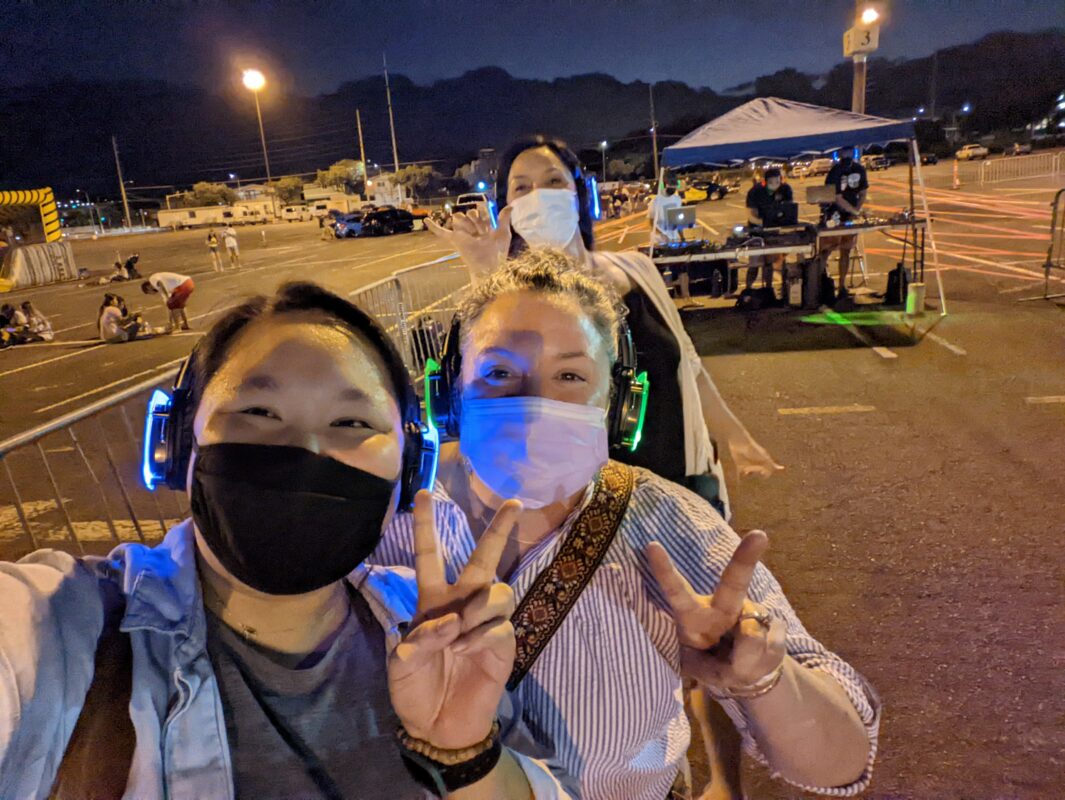 Three women wearing LED headphones and showing the peace sign.
