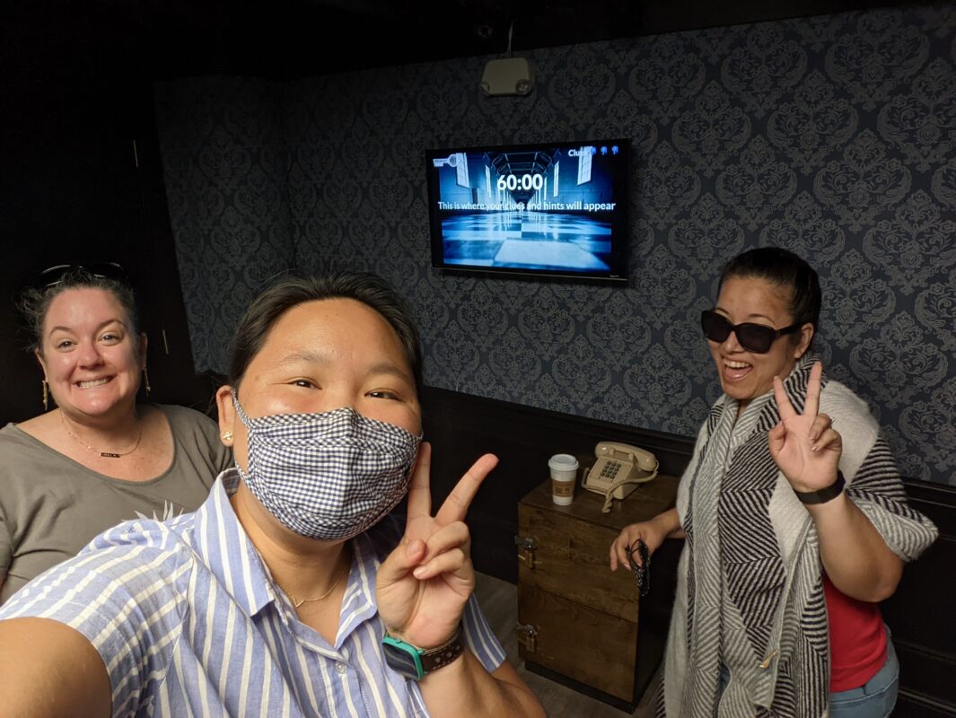 Three women smiling in front of a monitor.