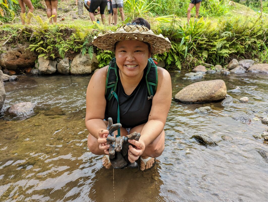 Woman kneeling in a river washing mud off.